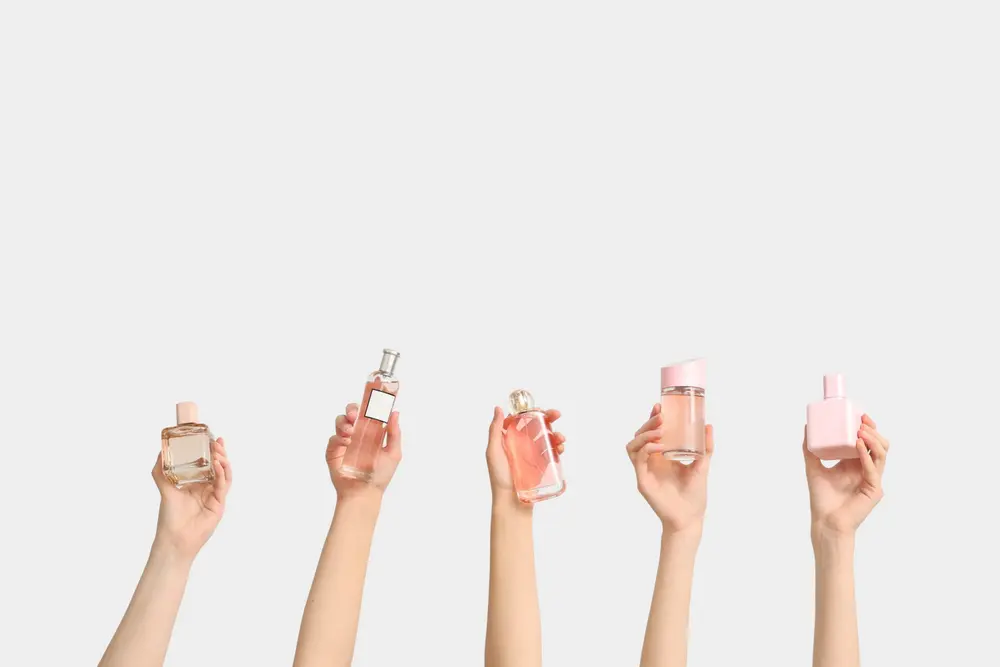 Layering de perfumes: por qué llevar varias fragancias a la vez es tendencia global Manos con botellas de perfume haciendo layering de perfumes