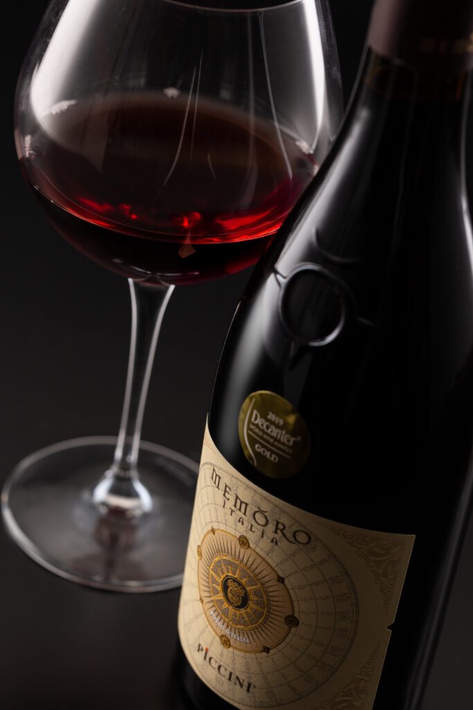 “colombia no es una apuesta, sino una historia que se extiende”, mario piccinni Copa de vino italiano en colombia servida al lado de una botella de vino memoro de piccini sobre un fondo oscuro.